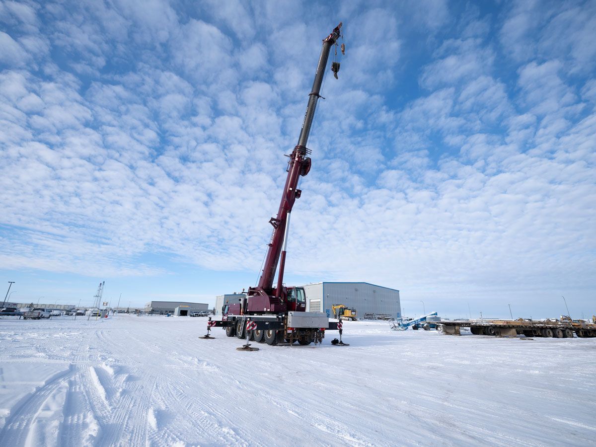 A large red crane on a snowy field with blue sky and white clouds, near buildings.
