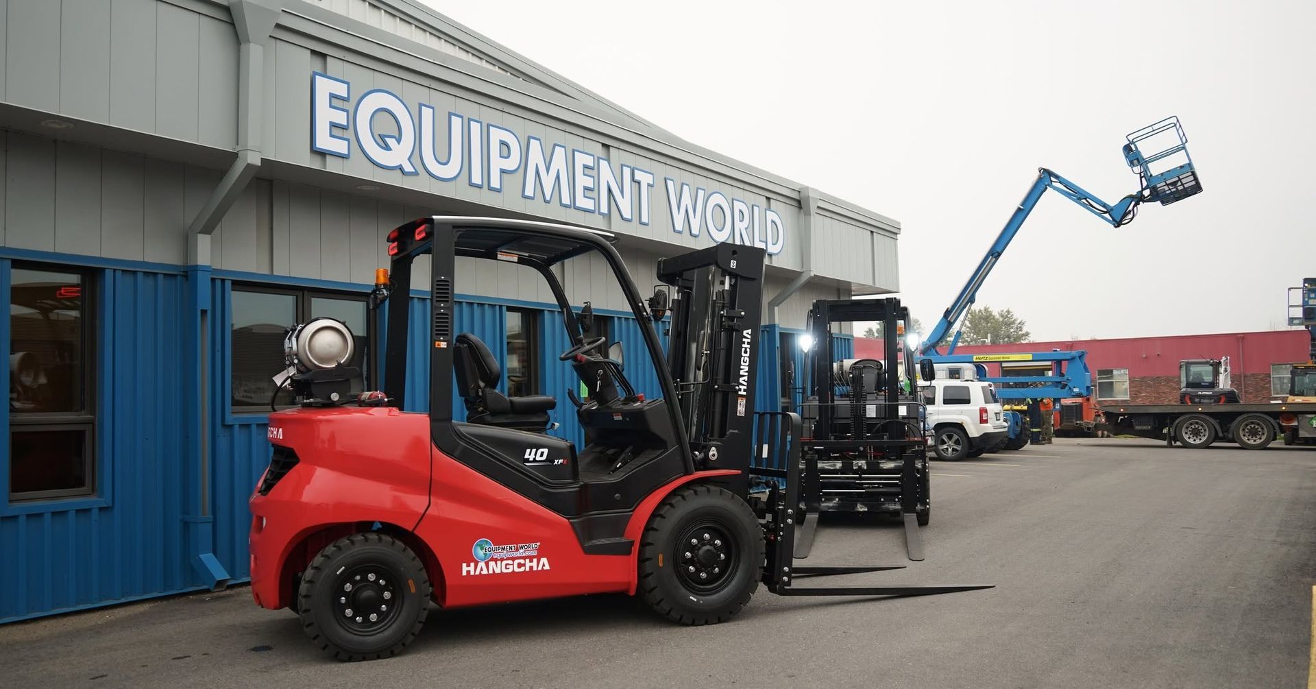 Red forklift parked outside Equipment World, with blue cherry picker and warehouse in background