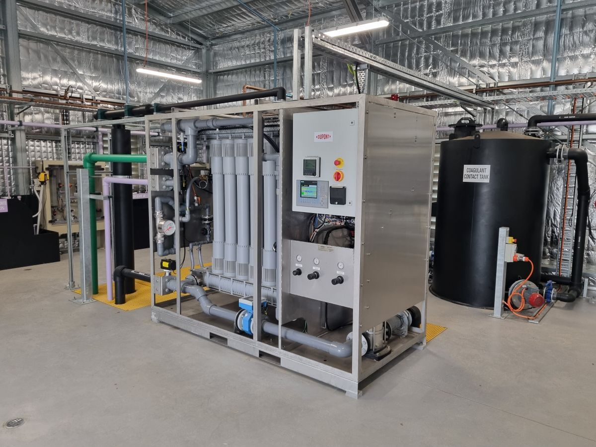 Industrial water treatment system in a large facility. Stainless steel equipment, black tank, and various pipes.