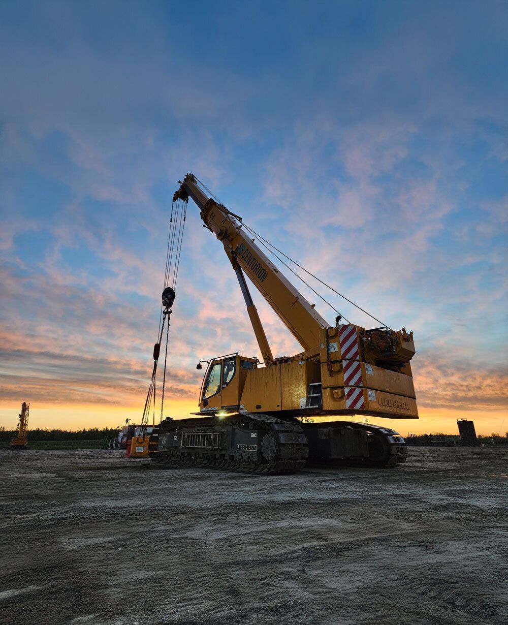 Yellow crawler crane on a construction site with an orange and blue sunset sky.