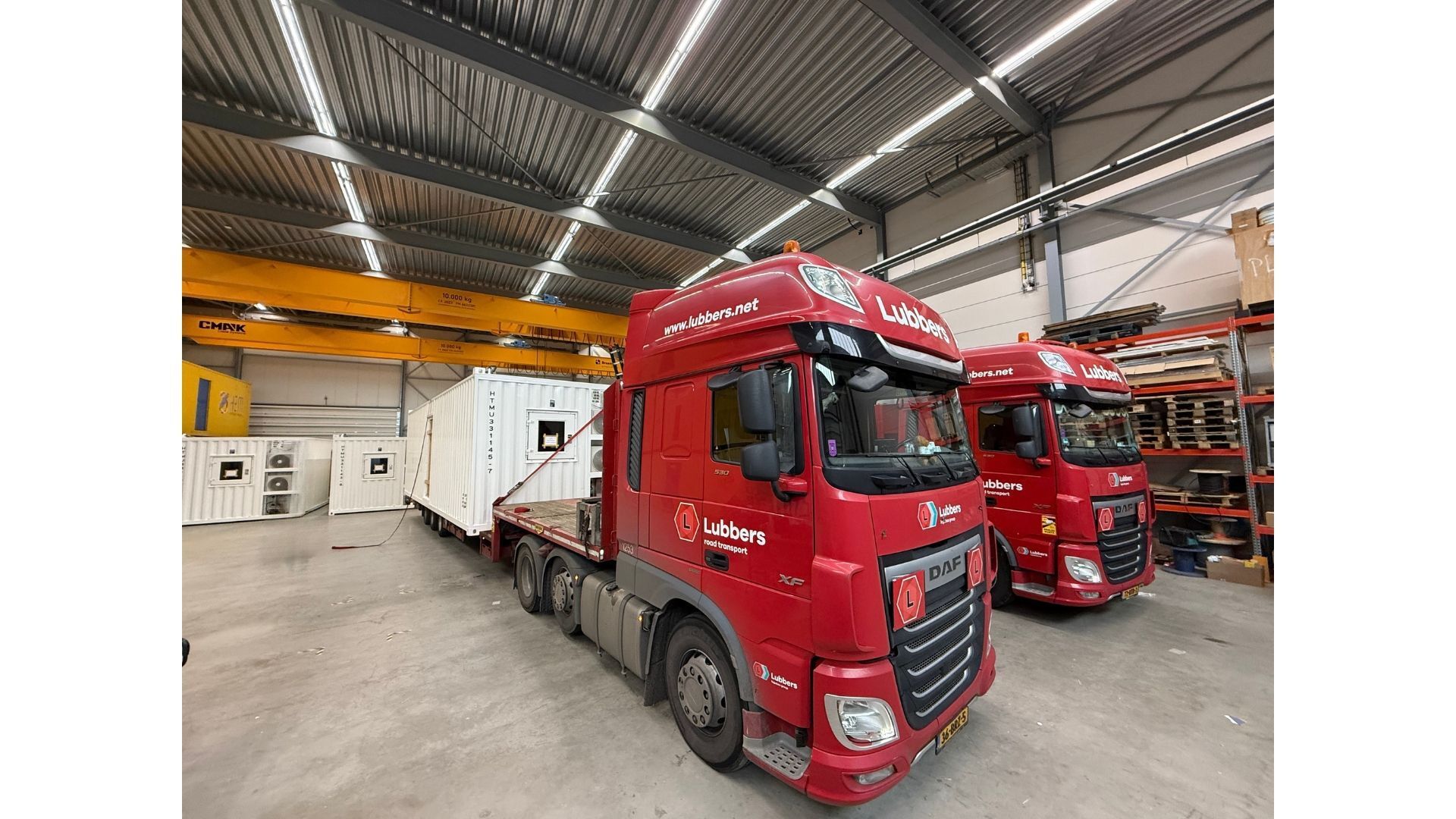 Red semi-truck parked inside a warehouse with other red trucks and industrial shelving.