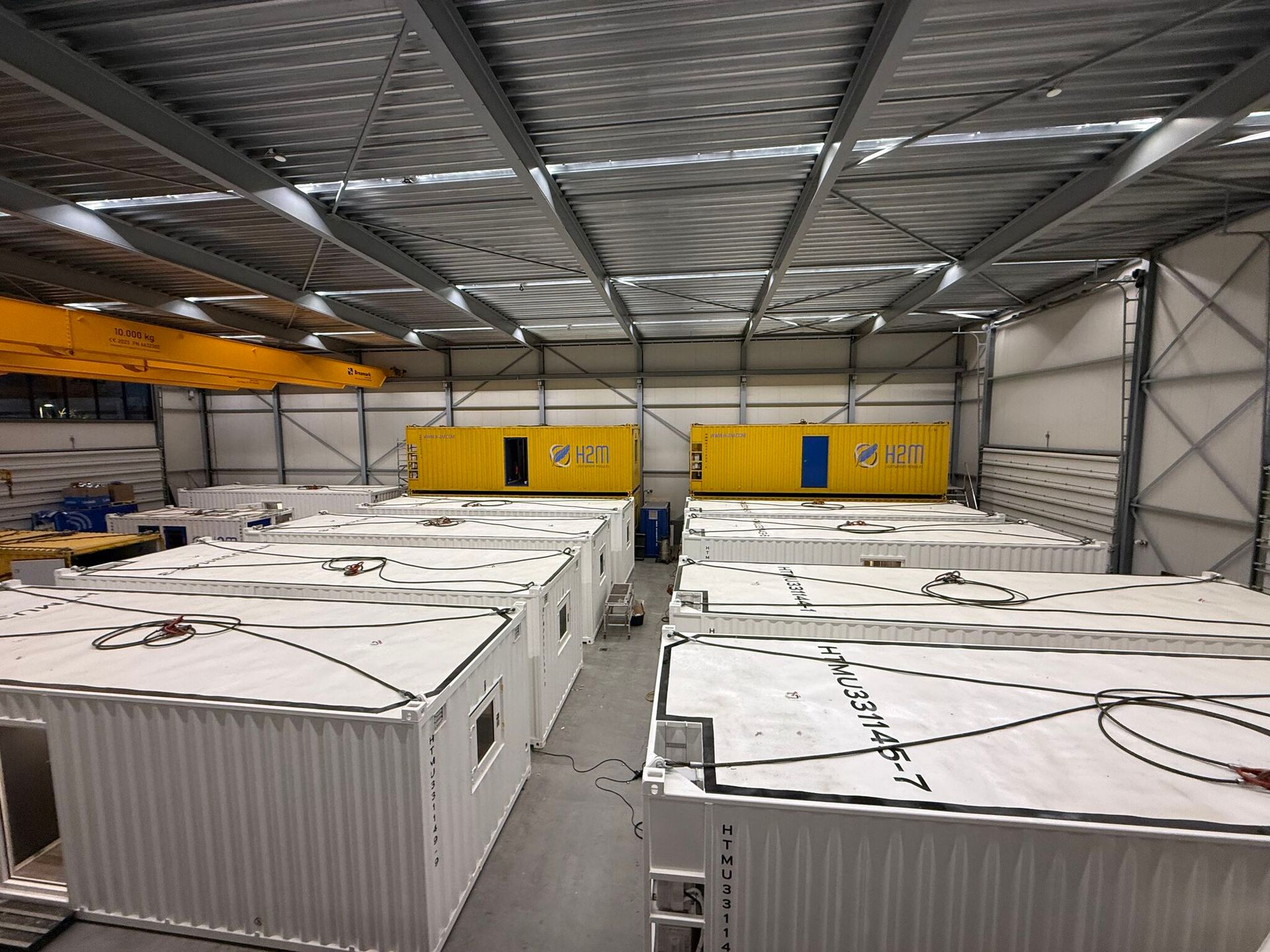 Warehouse with rows of white cargo containers under a metal roof, yellow doors in the back wall