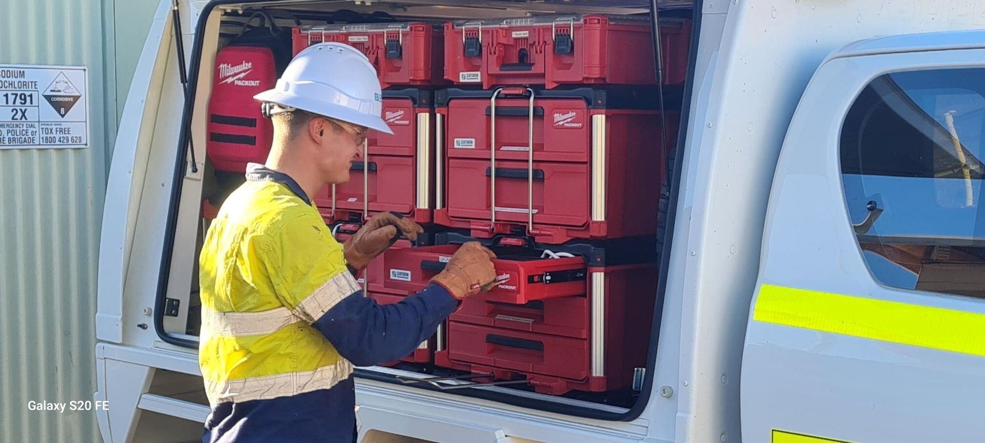 A worker in safety gear organizes red toolboxes in the back of a truck.