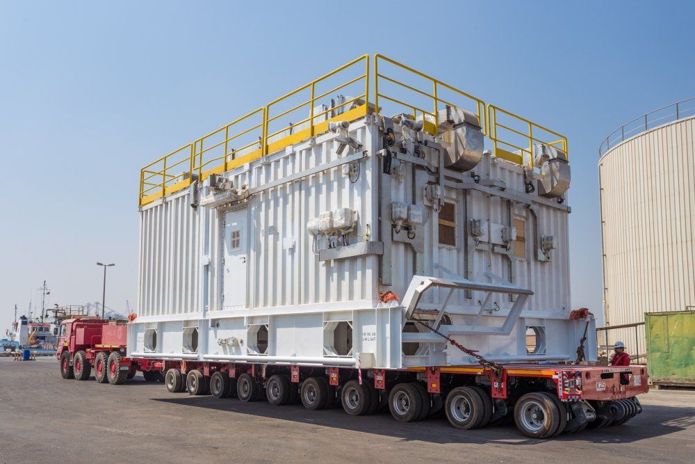Large white industrial unit on a multi-axle trailer, outdoors on a sunny day.