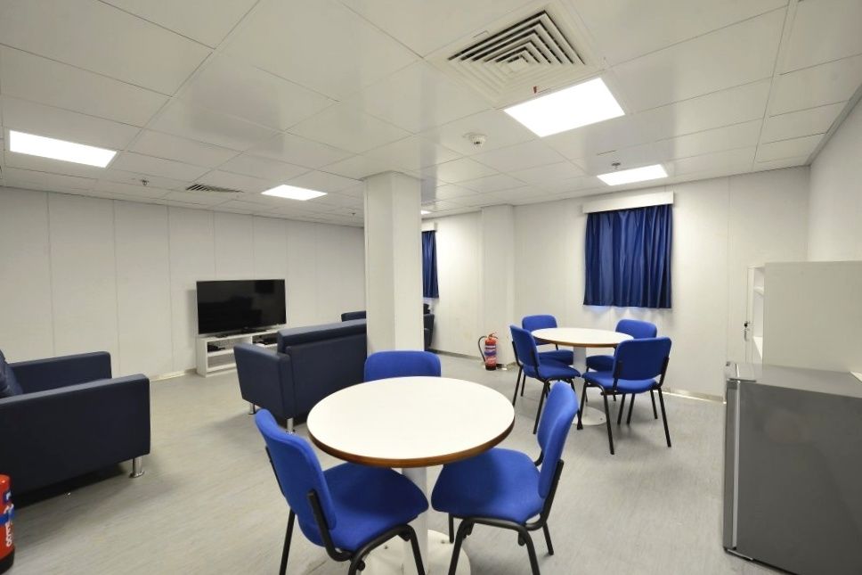 An empty, modern break room with blue furniture, tables, a TV, and a fire extinguisher.