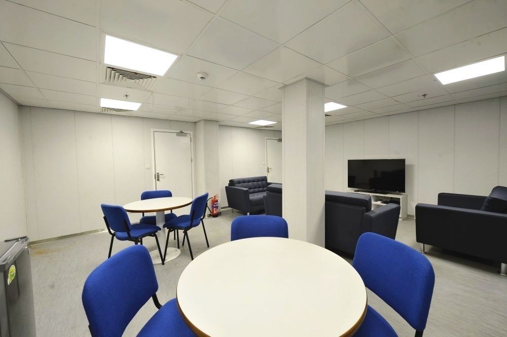 A small, modern lounge with round tables, blue chairs, dark blue armchairs, and a TV.