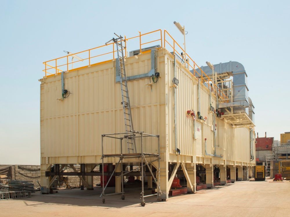 Large beige industrial building with scaffolding and piping outdoors.