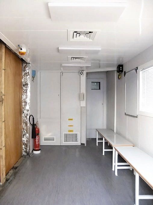 Interior of a small, white room with benches, a cabinet, and a fire extinguisher.