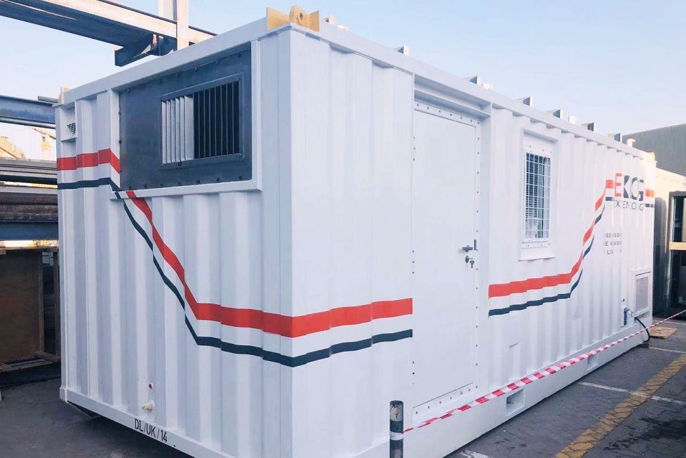 White portable office container with black and red accents, a window, and a door, outdoors.