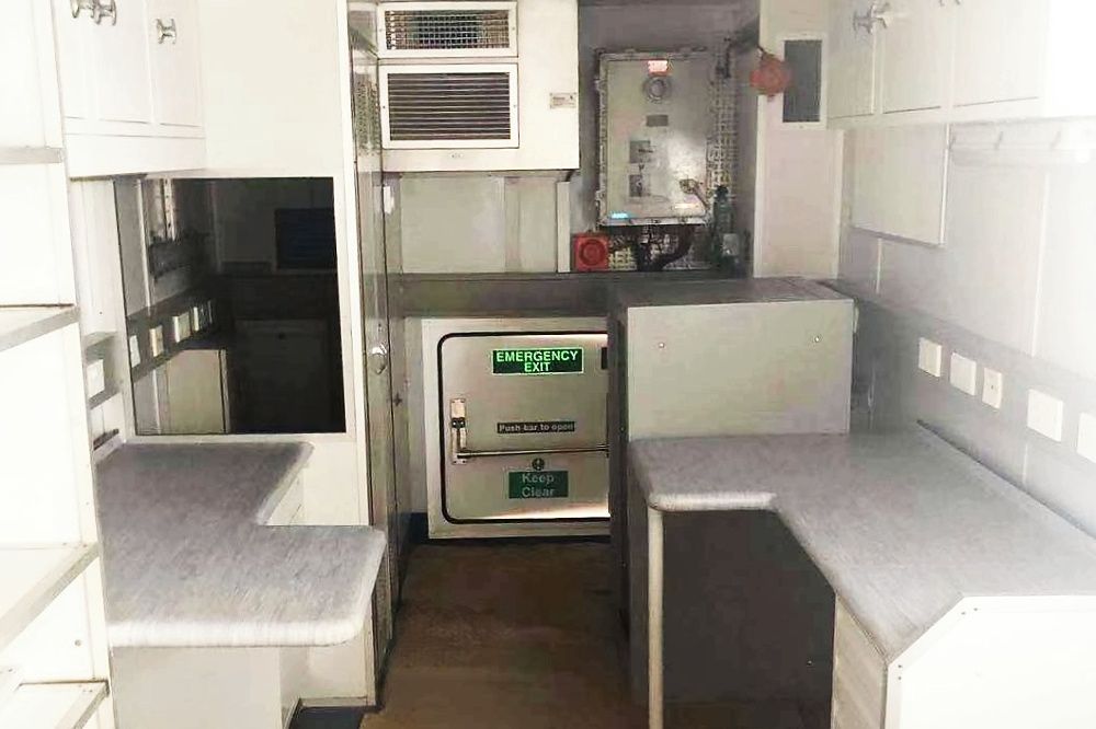 Interior of a mobile medical unit with cabinets, counters, and equipment; white and gray color scheme.