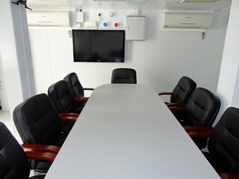 Conference room with large white table, black chairs, and a mounted TV.