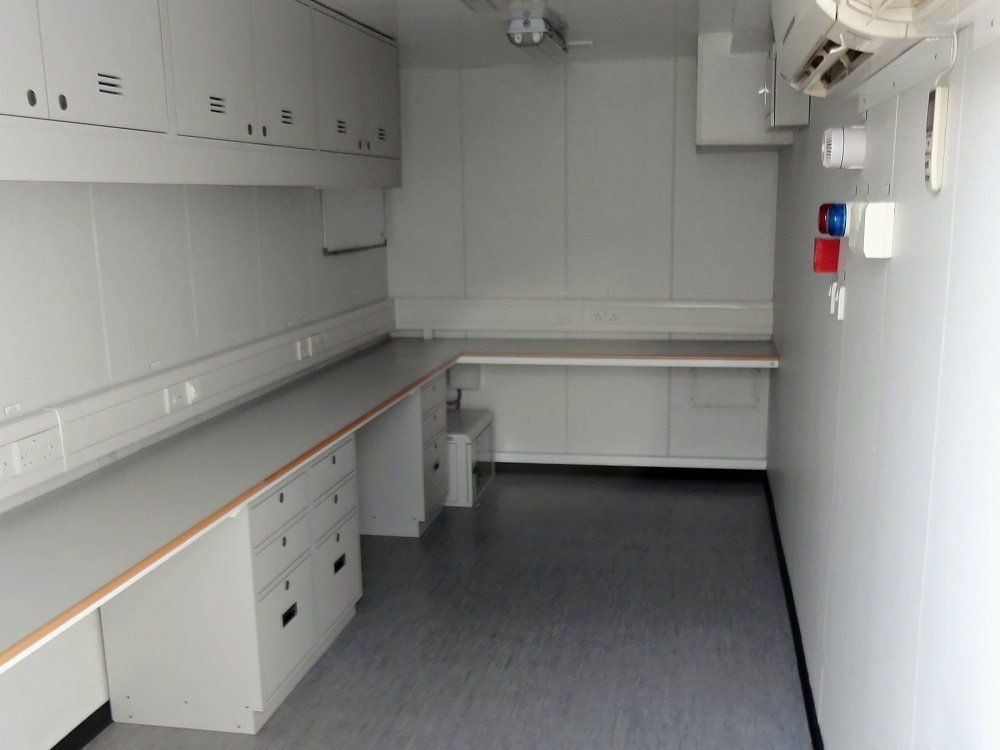 Interior of a white laboratory-like space with countertops, cabinets, and a gray floor.