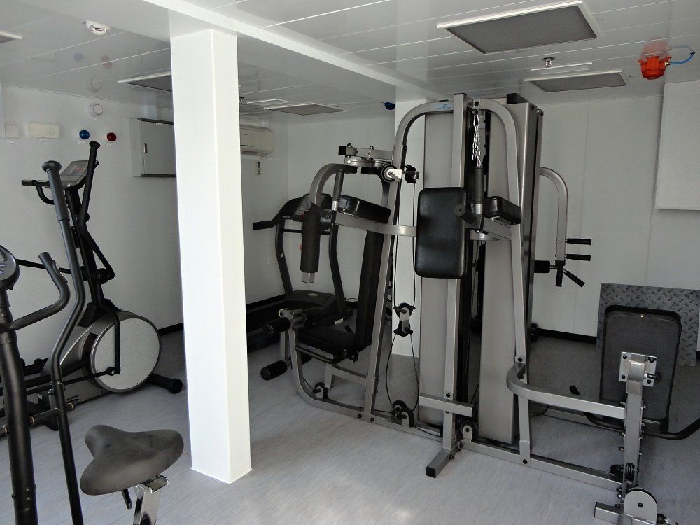 Gym with exercise equipment. Includes treadmill, elliptical machine, and multi-station weight machine. Bright interior.