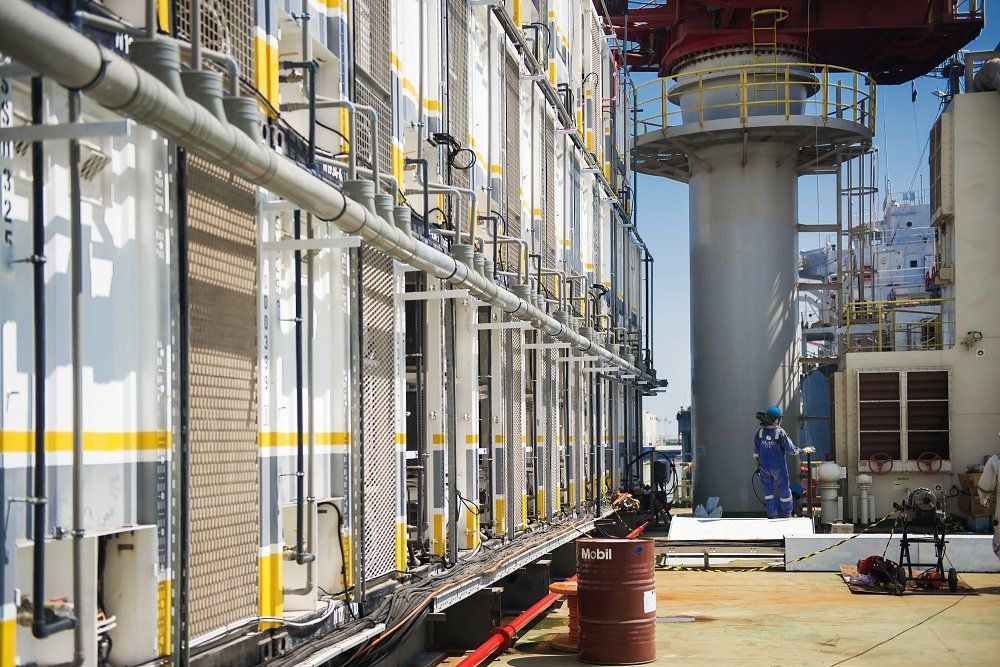 Industrial site with metal containers, piping, and a worker in blue.