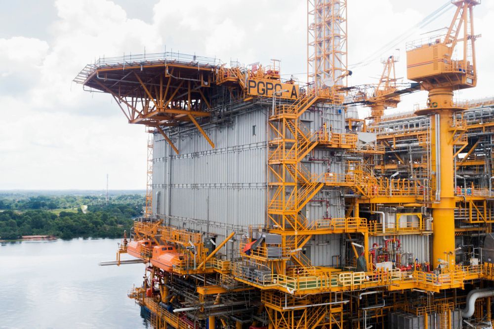 Offshore oil and gas platform with yellow framework and helipad against a cloudy sky.