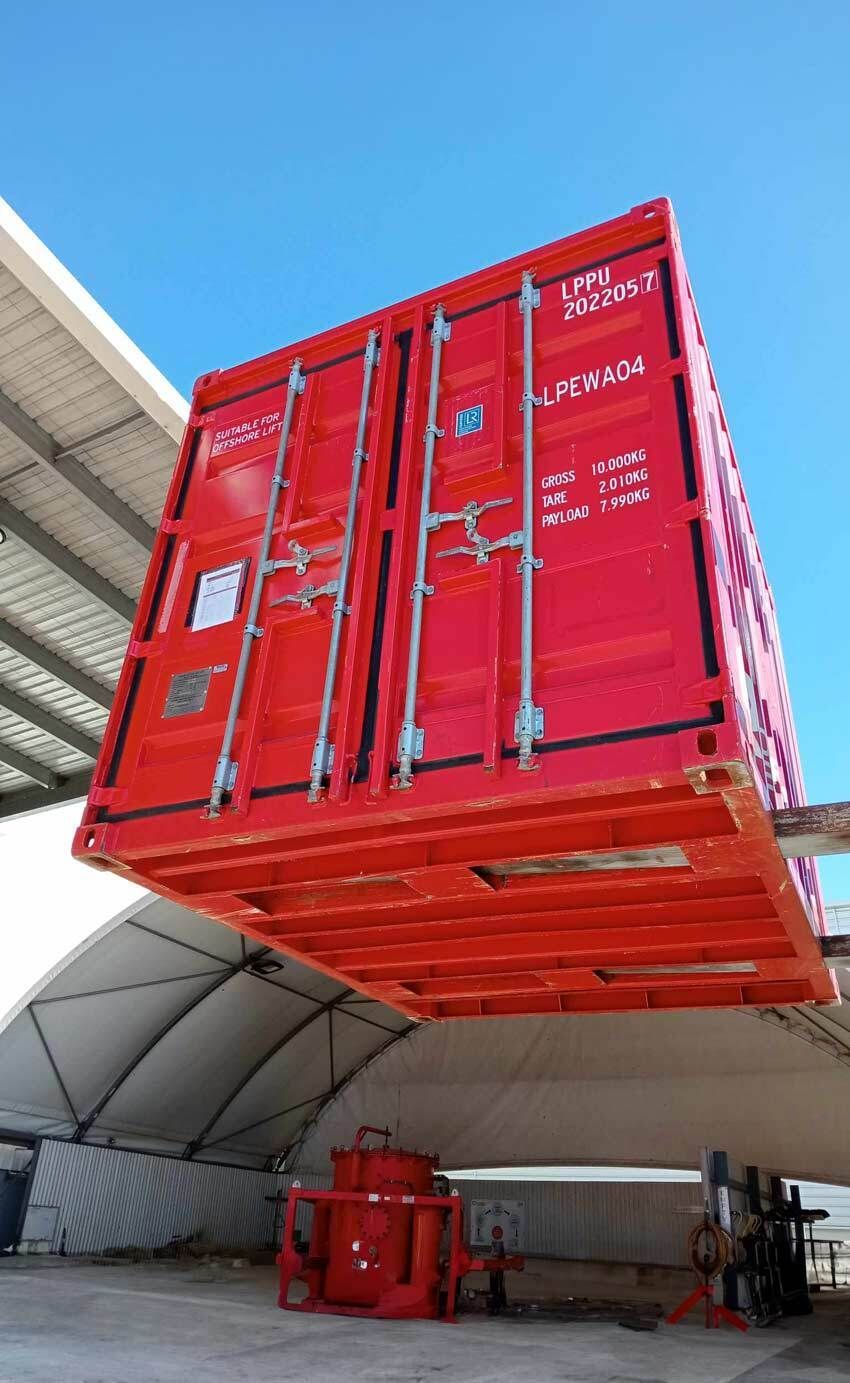 Red shipping container suspended above a white tent, blue sky in the background.