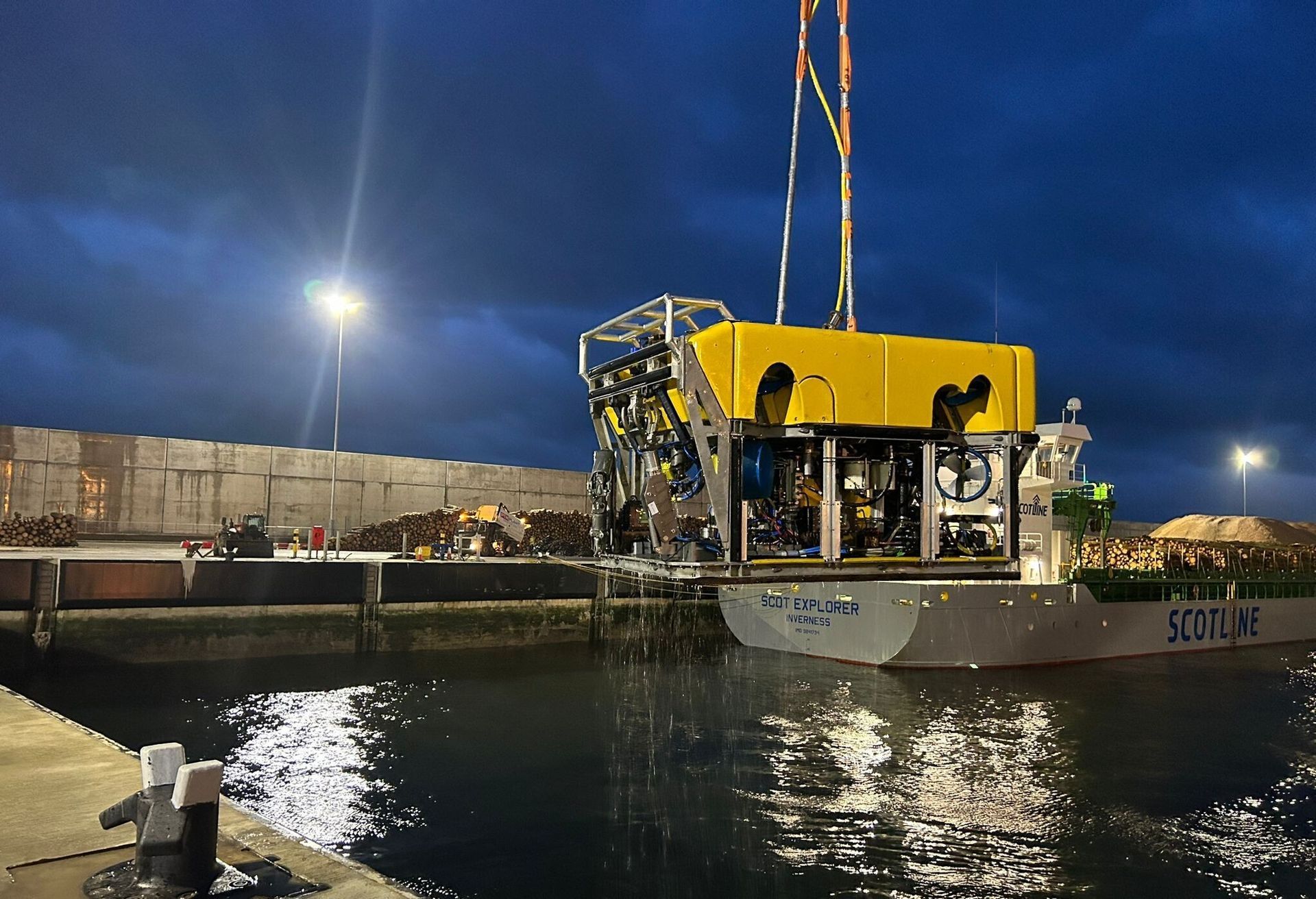 A yellow submersible is lifted from a boat at a dock at dusk.