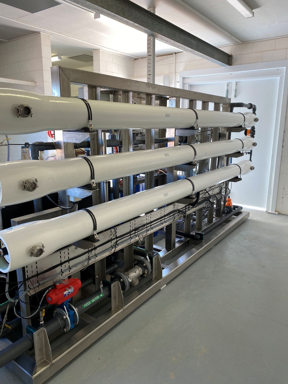 Water filtration system in a clean, bright room. Cylindrical white filters on metal framework.