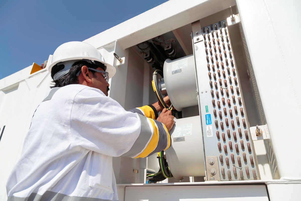Technician in white hard hat providing facilities manangement services inside an outdoor utility cabinet