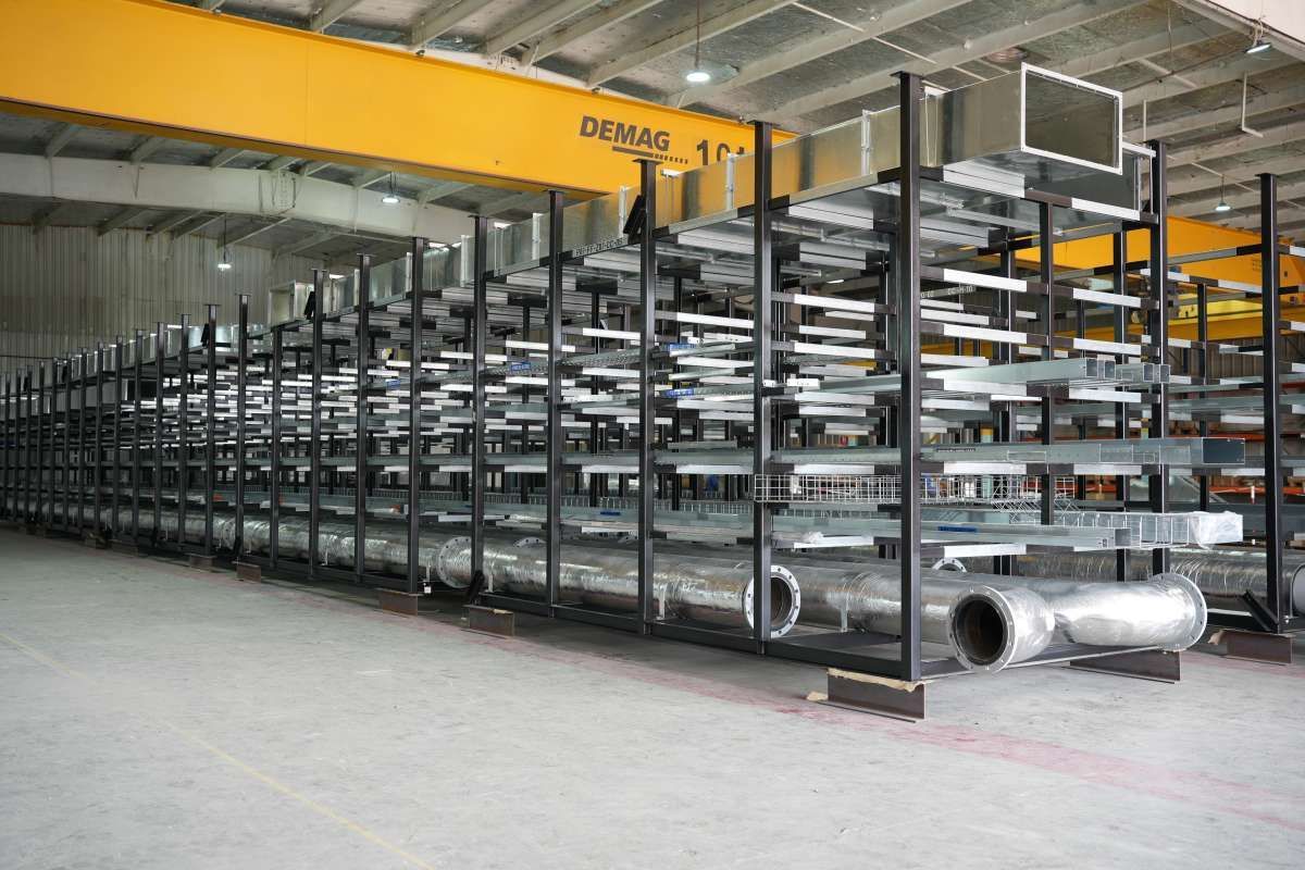 Centurion warehouse with metal storage racks holding large silver pipes under yellow overhead crane