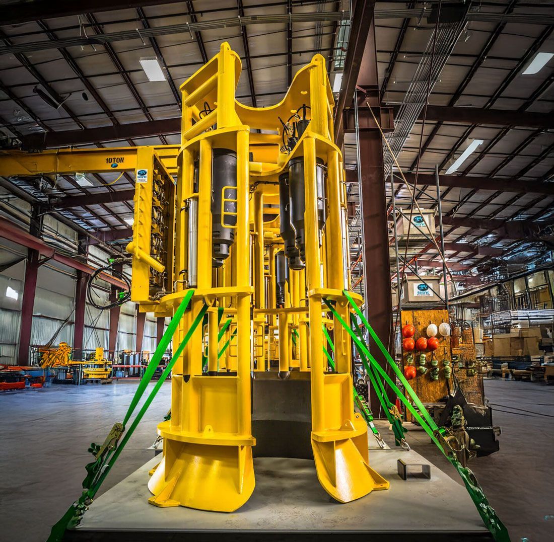 Large yellow industrial machine secured with green straps inside a warehouse.