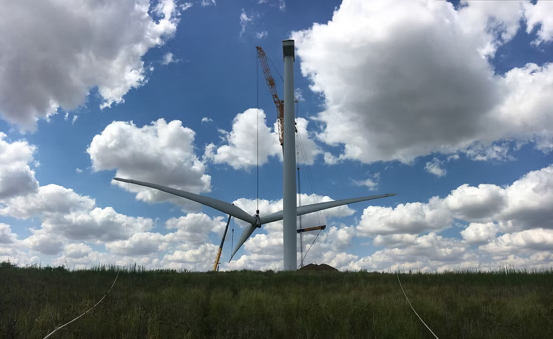Wind turbines in a grassy field under a blue sky with large white clouds with Centurion Cranes providing maintenance services