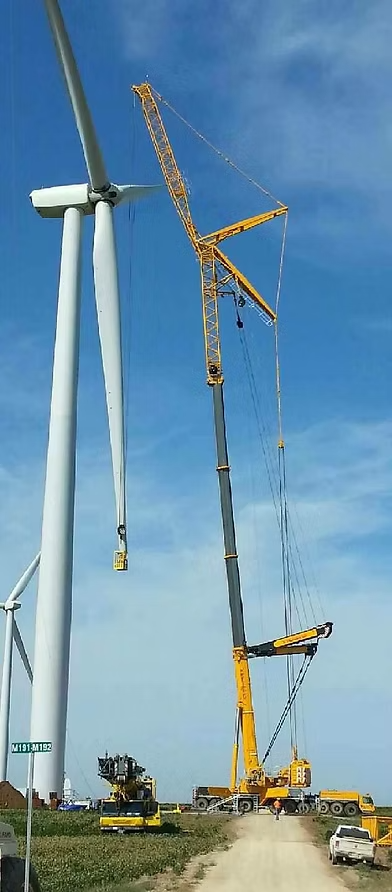 Two wind turbines being maintained by large yellow Centurion cranes on a grassy site under a blue sky