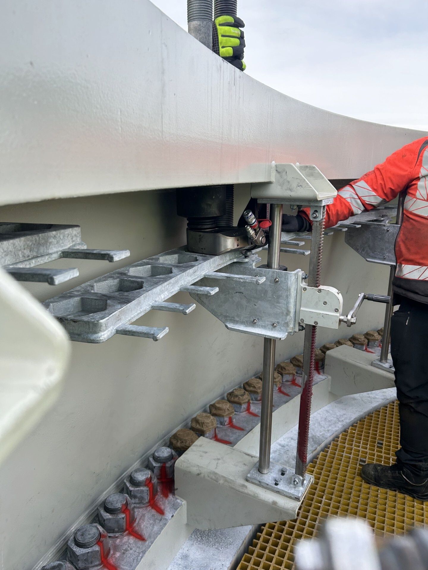 Person in orange vest operates machinery near a large, industrial structure with metal components.