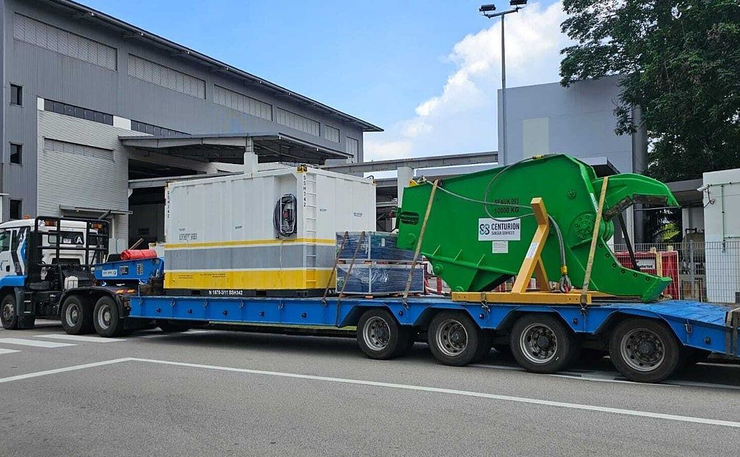 Green subsea sheer and accommodation module on a blue multi-axle trailer outside a warehouse