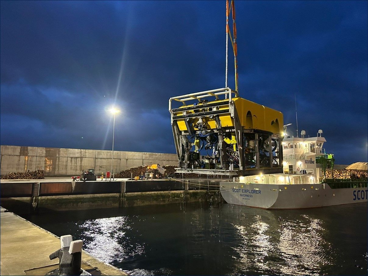 A yellow submersible is lifted from a ship at a port at night.