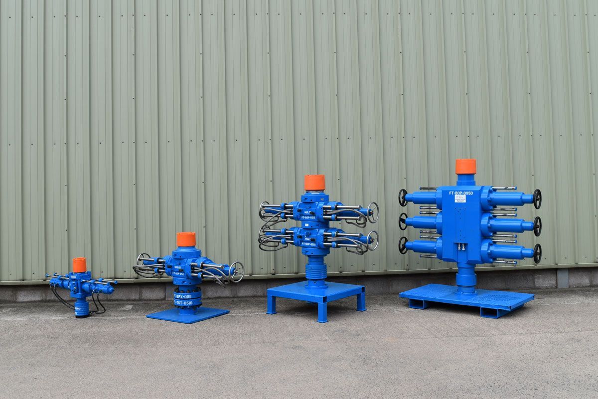 Four blue wellhead Christmas trees, varying sizes, set against a light green building wall.