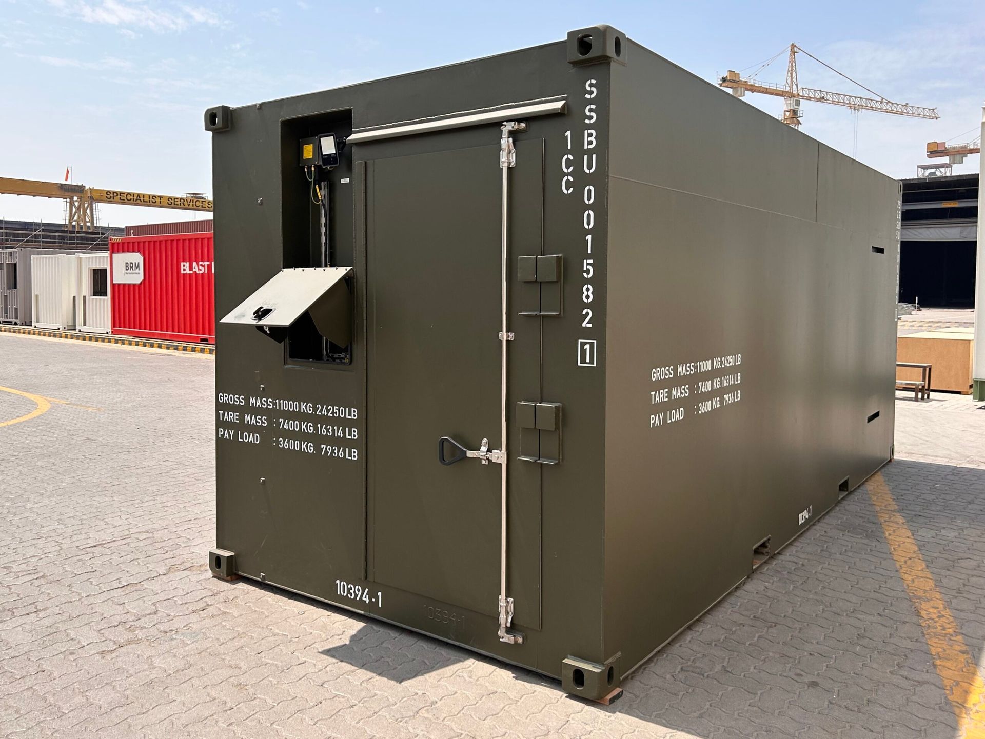 Green shipping container with a door and side panel labels, in an outdoor setting.