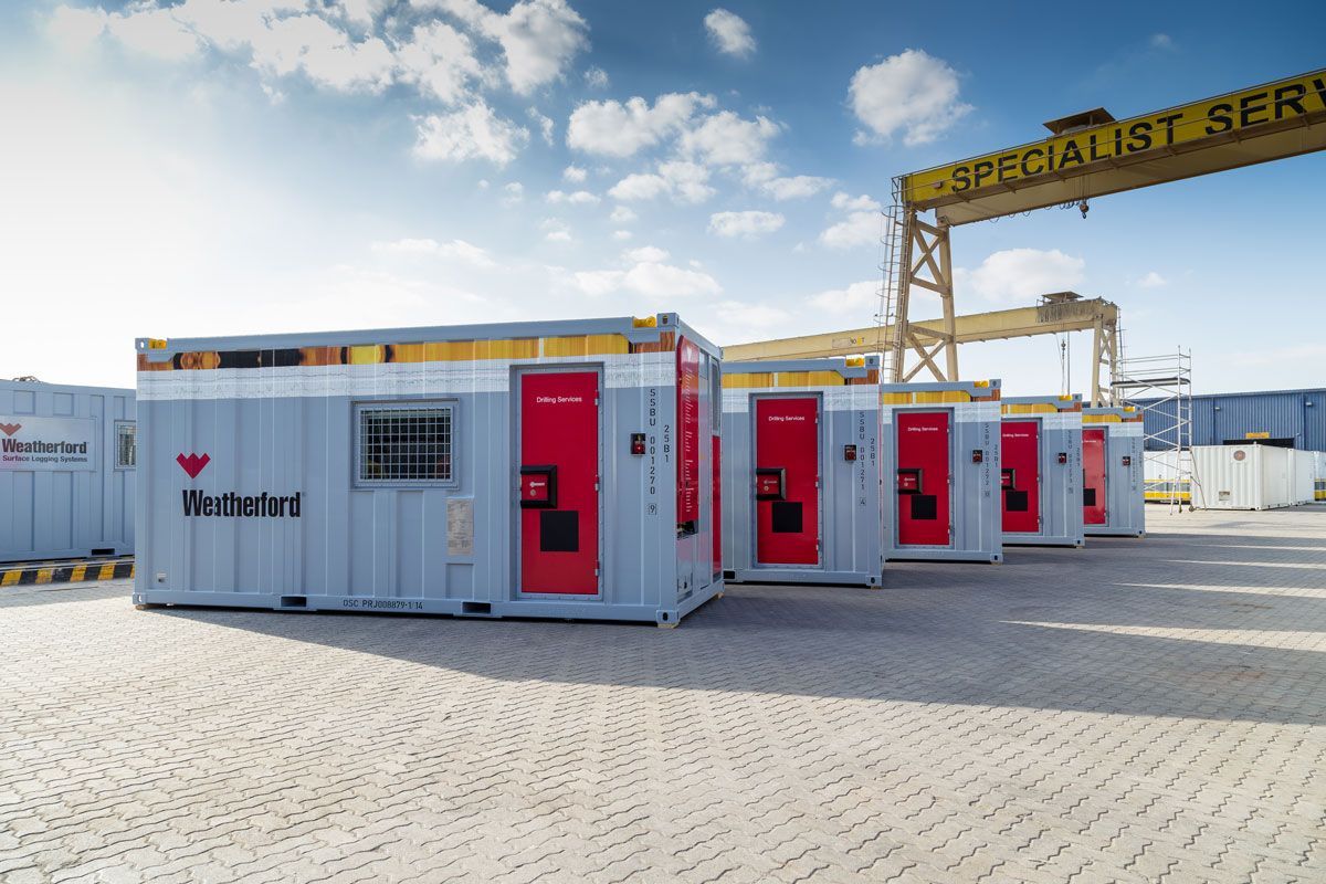 White modular buildings with red doors in an industrial yard under a crane