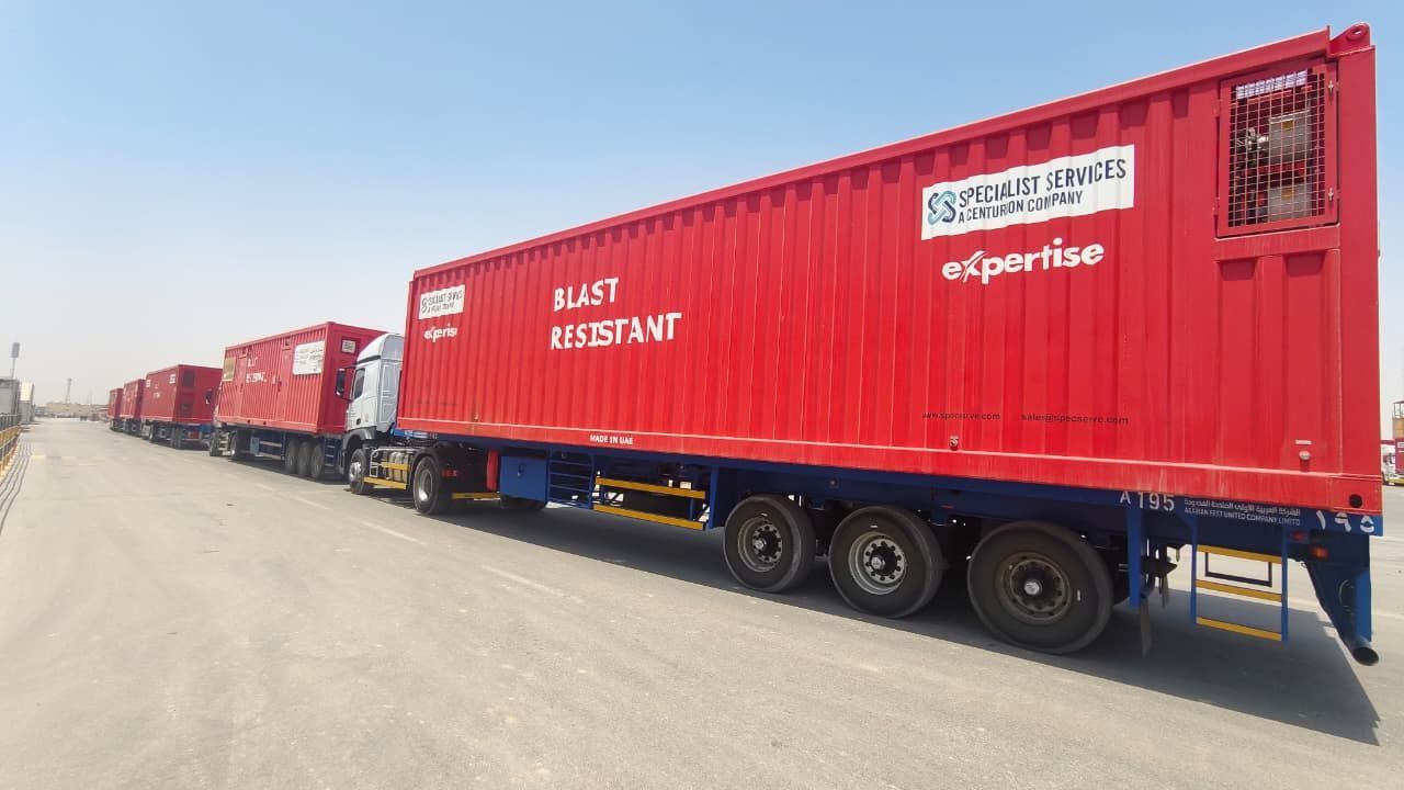 Red Centurion Specialist  Services blast resistant modules on trailers  on a dusty road in daylight