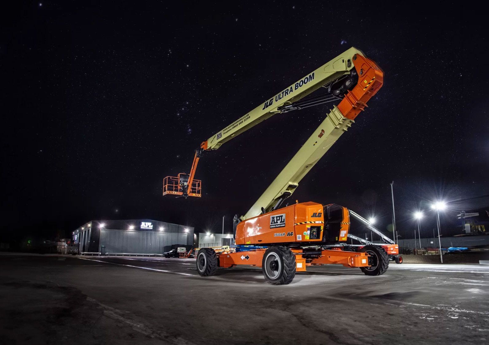 Orange mobile APL crane lifts a work platform at a construction site at night