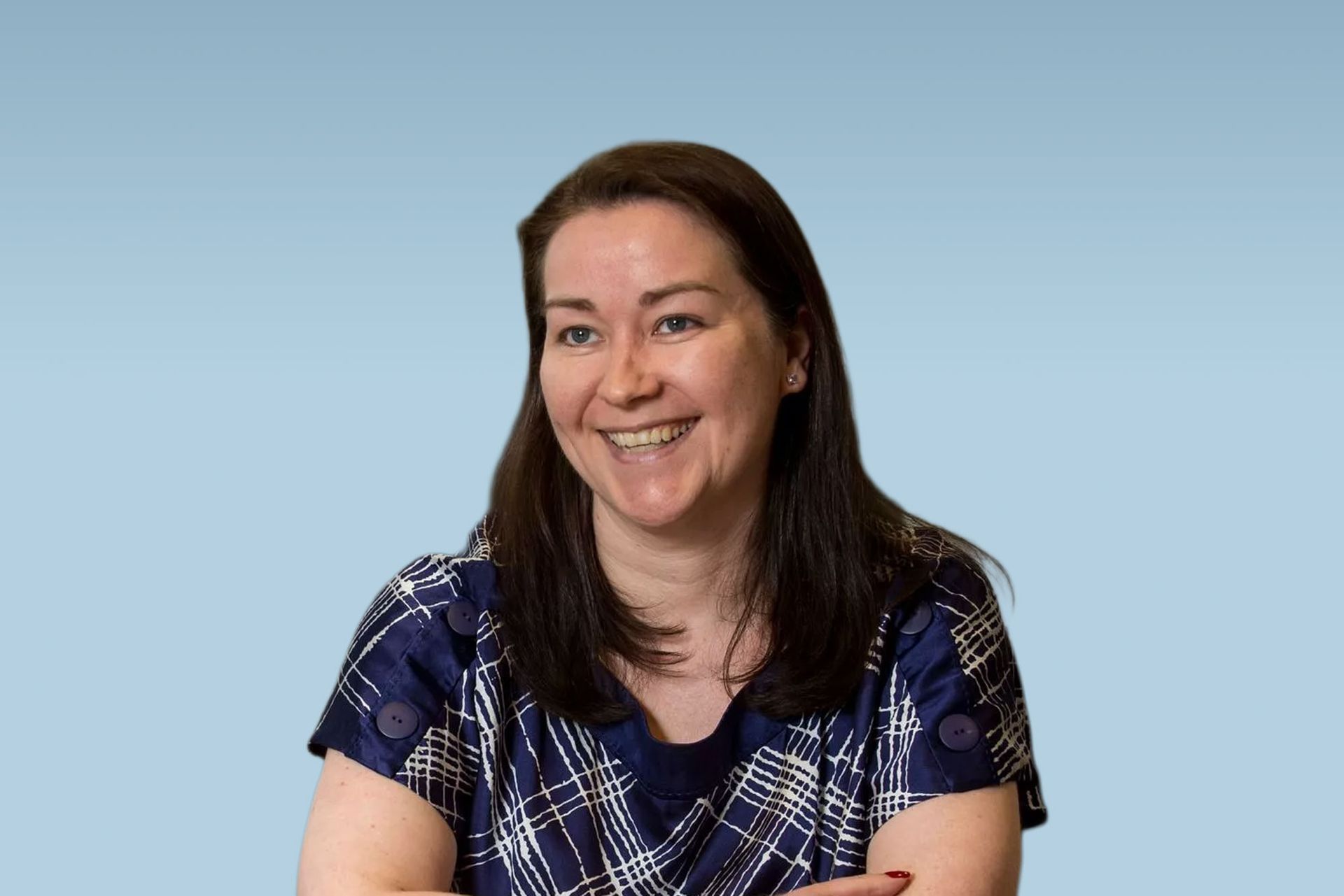 Woman with fair skin smiling, wearing a dark blue shirt and lanyard, in front of a blurred city view.