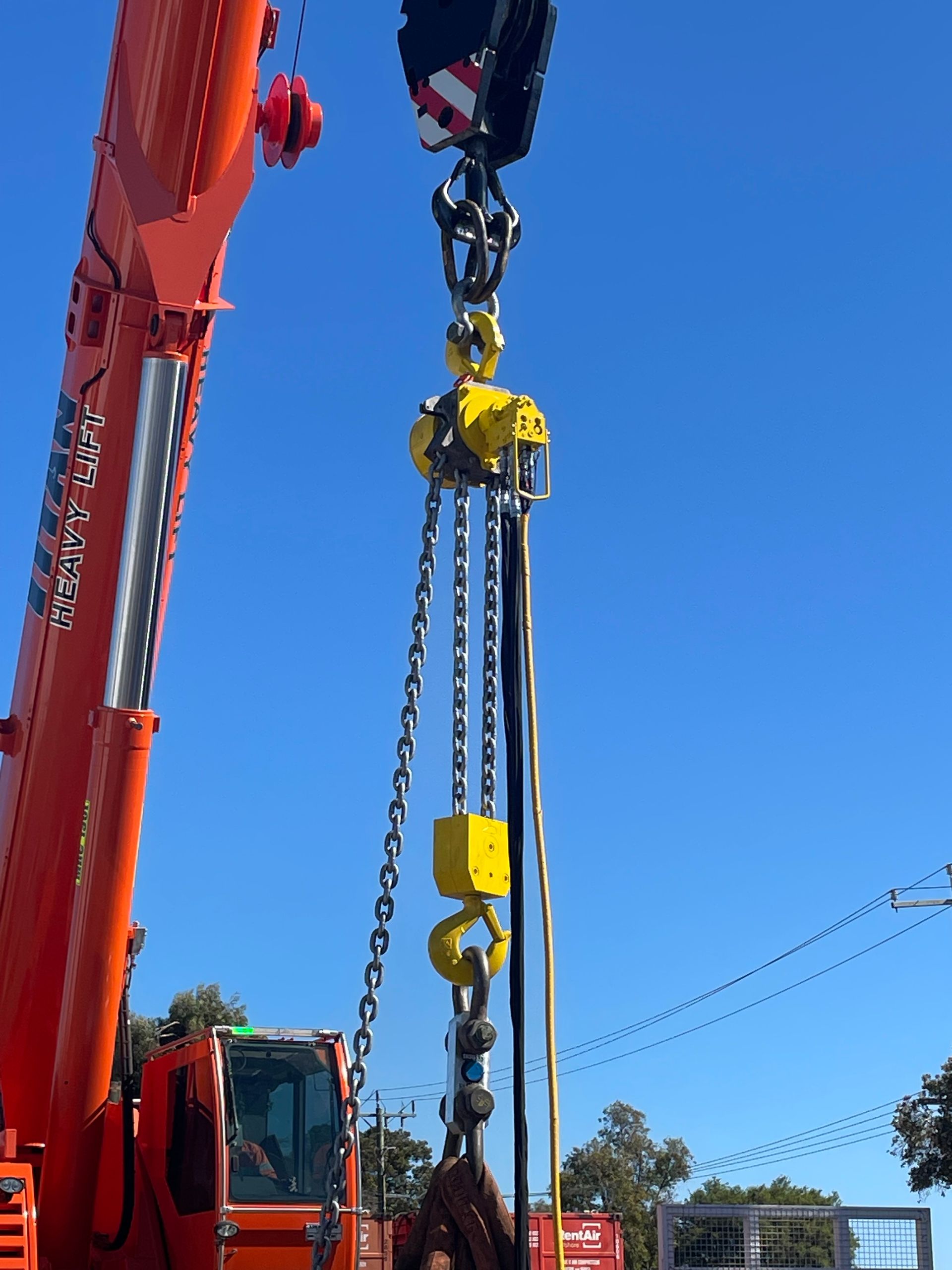 Orange Centurion crane lifting a heavy chain rig with yellow hooks against a clear blue sky