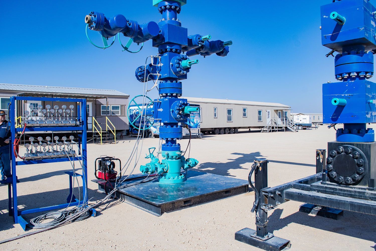 Blue wellhead equipment in an outdoor setting with support structures and a clear sky.
