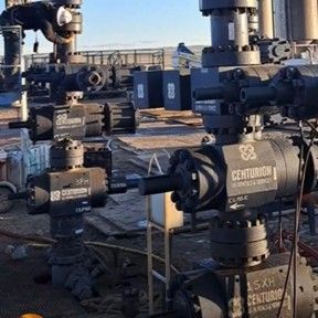 Oil field equipment with black valves and pipes, outdoors. Centurion brand is visible on the valves.