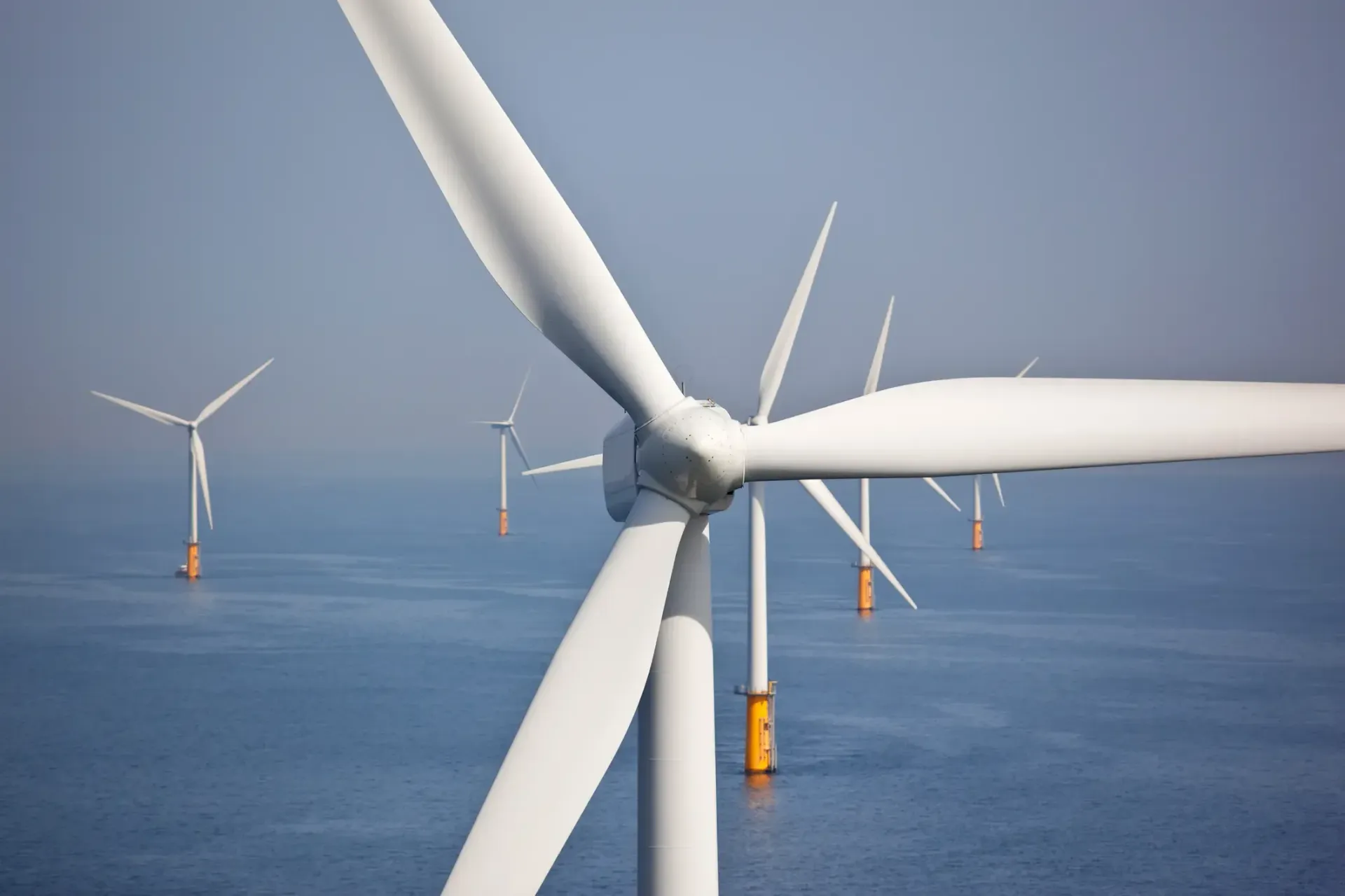 Wind turbines generating power over a calm blue ocean at sea.