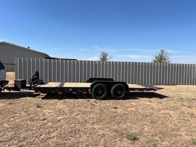A flatbed trailer is parked in a field next to a fence.