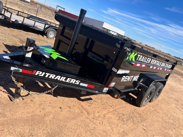A dump trailer with pj trailers written on the side is parked in the dirt.