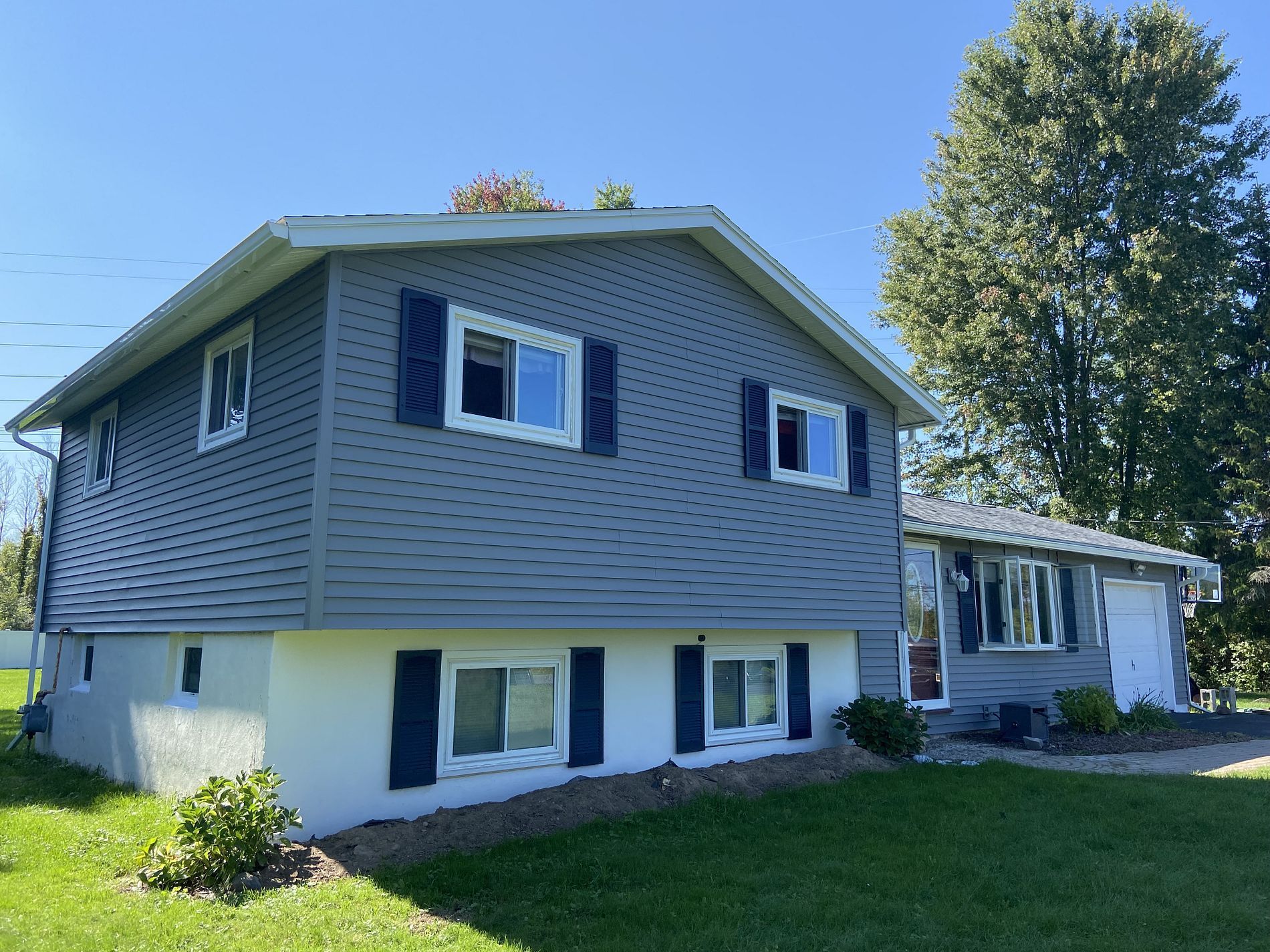Two-story house with blue-gray siding, white trim, and navy shutters. A sunny day with green lawn and trees.