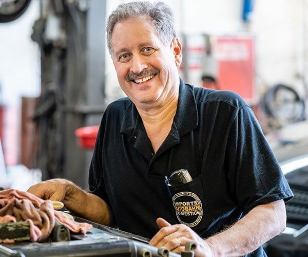 A man is smiling while working on a car in a garage.