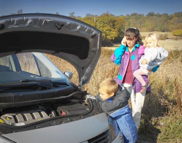 A woman and two children are looking under the hood of a broken down car.