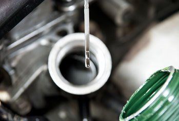 A close up of a person pouring oil into a car engine.