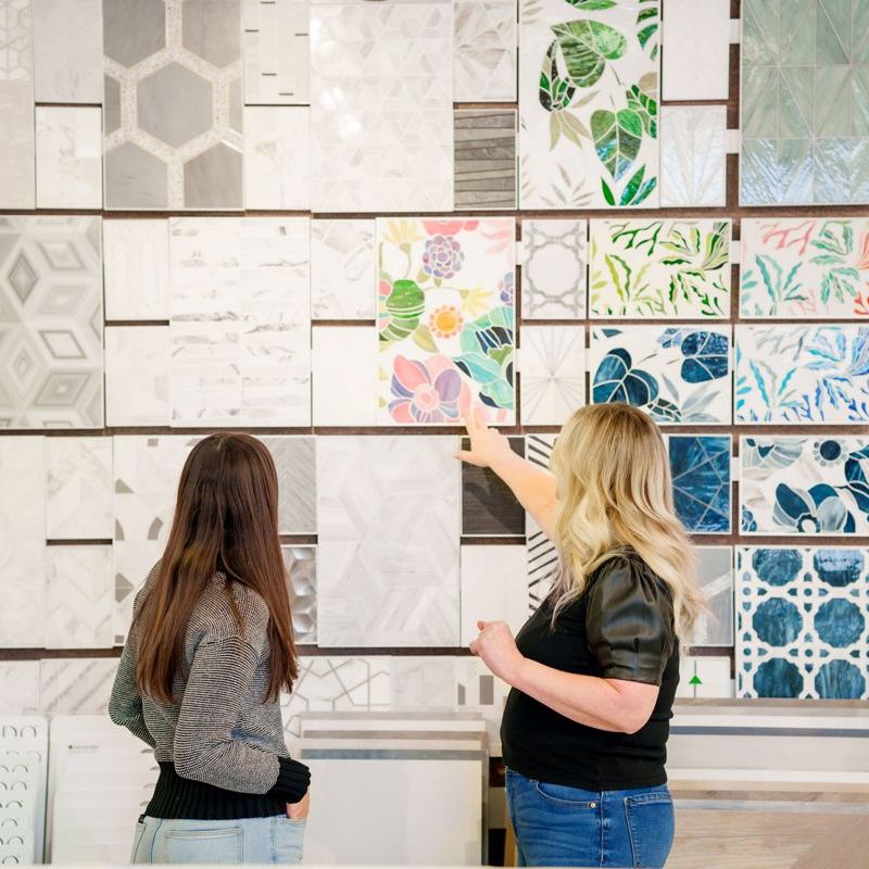 Two women are looking at a wall of tiles in a store.