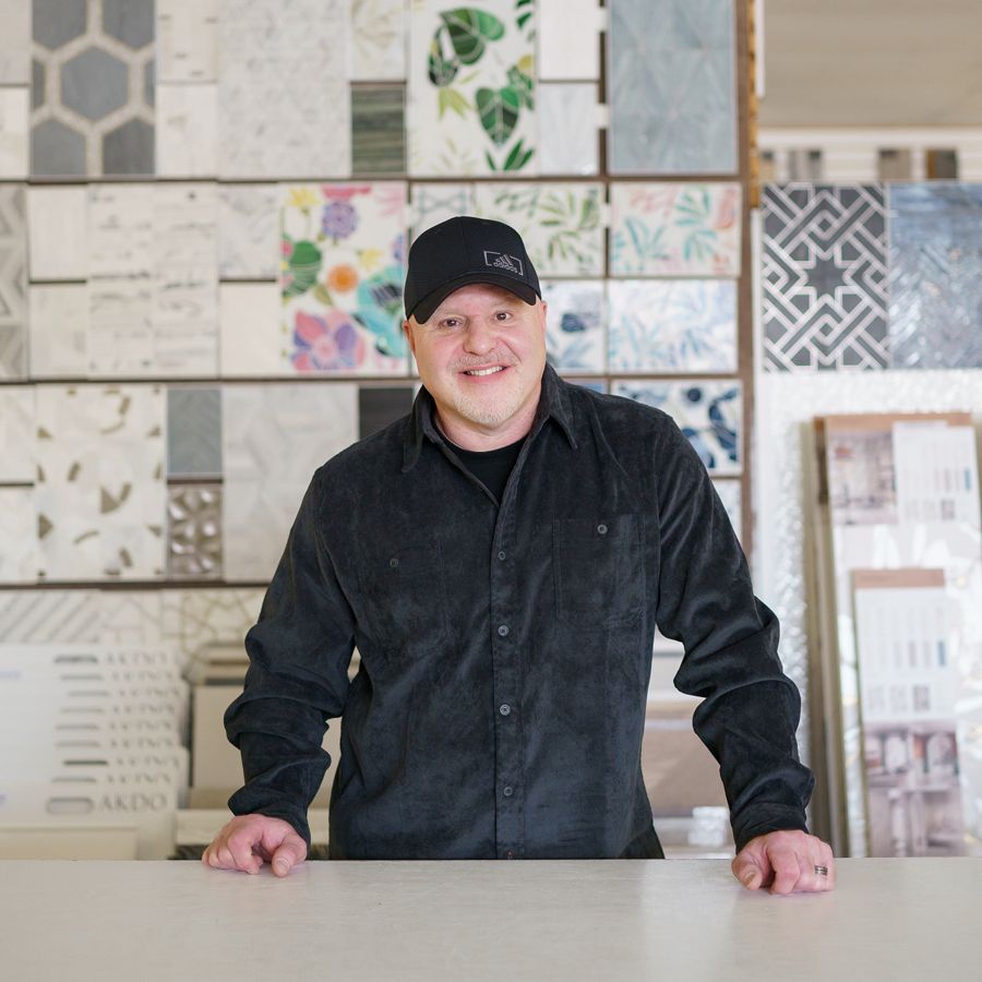 A man wearing a black hat and a black shirt is standing in front of a wall of tiles