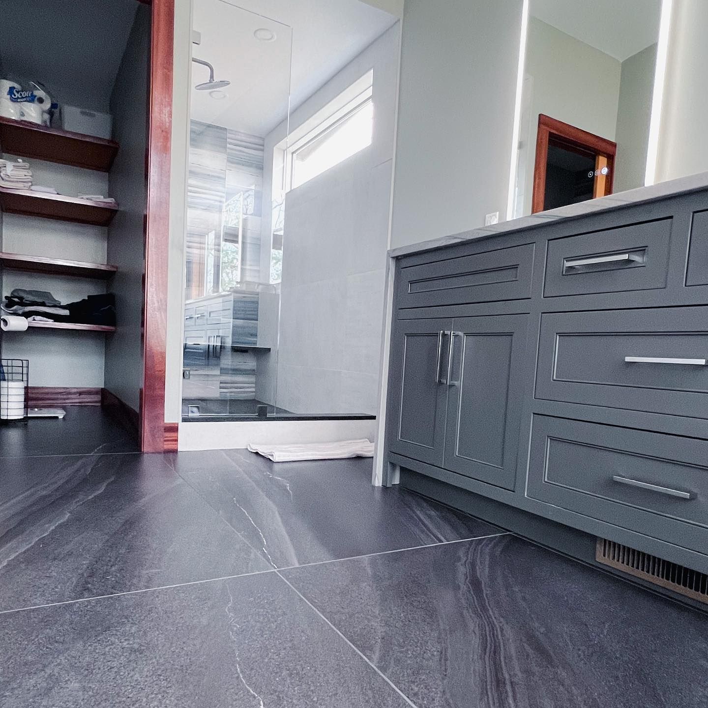 A bathroom with gray cabinets and a walk in shower