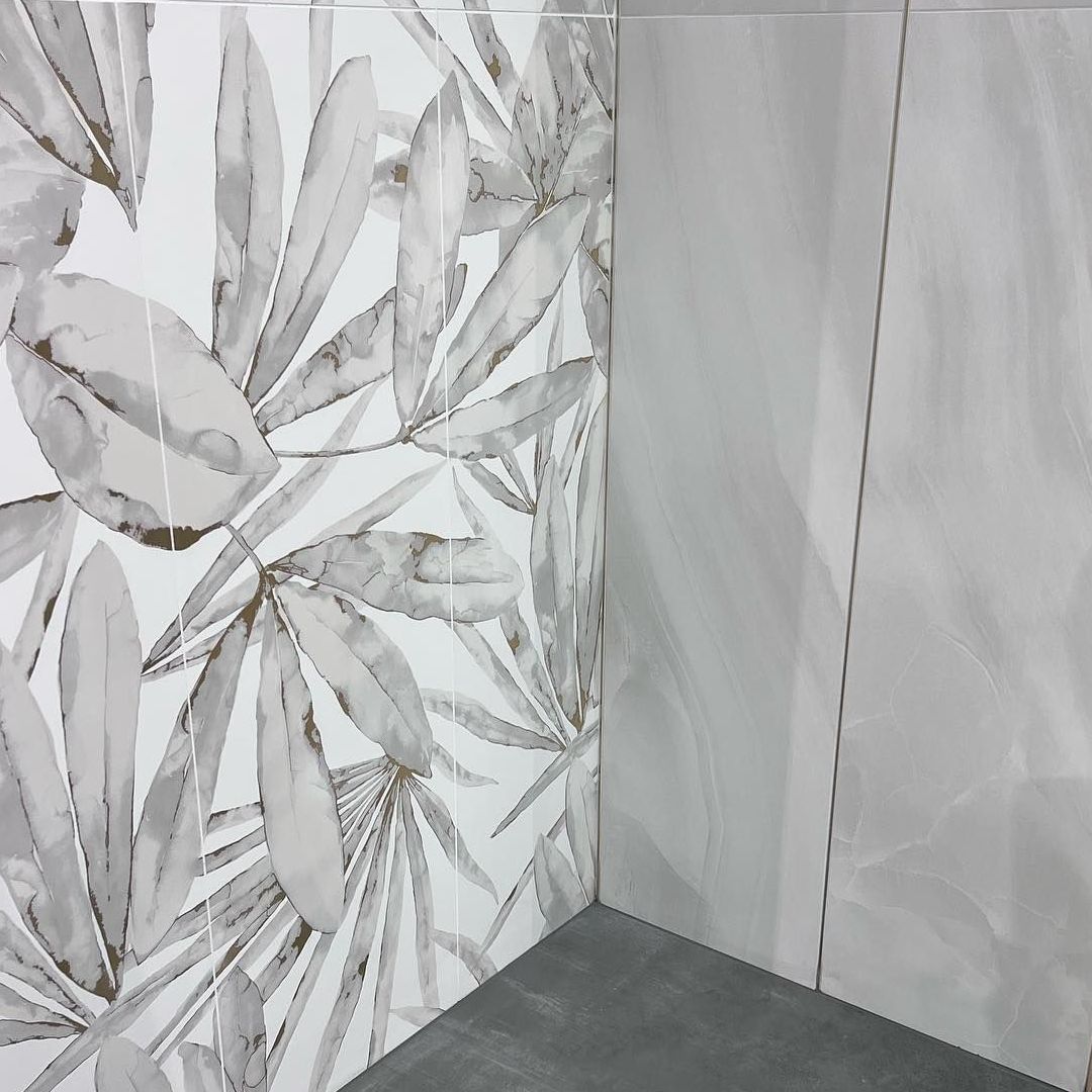A corner of a bathroom with a tile wall with leaves on it